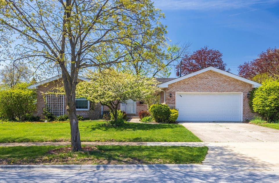 Brick single-story home with a wide front lawn, mature trees and an attached two-car garage